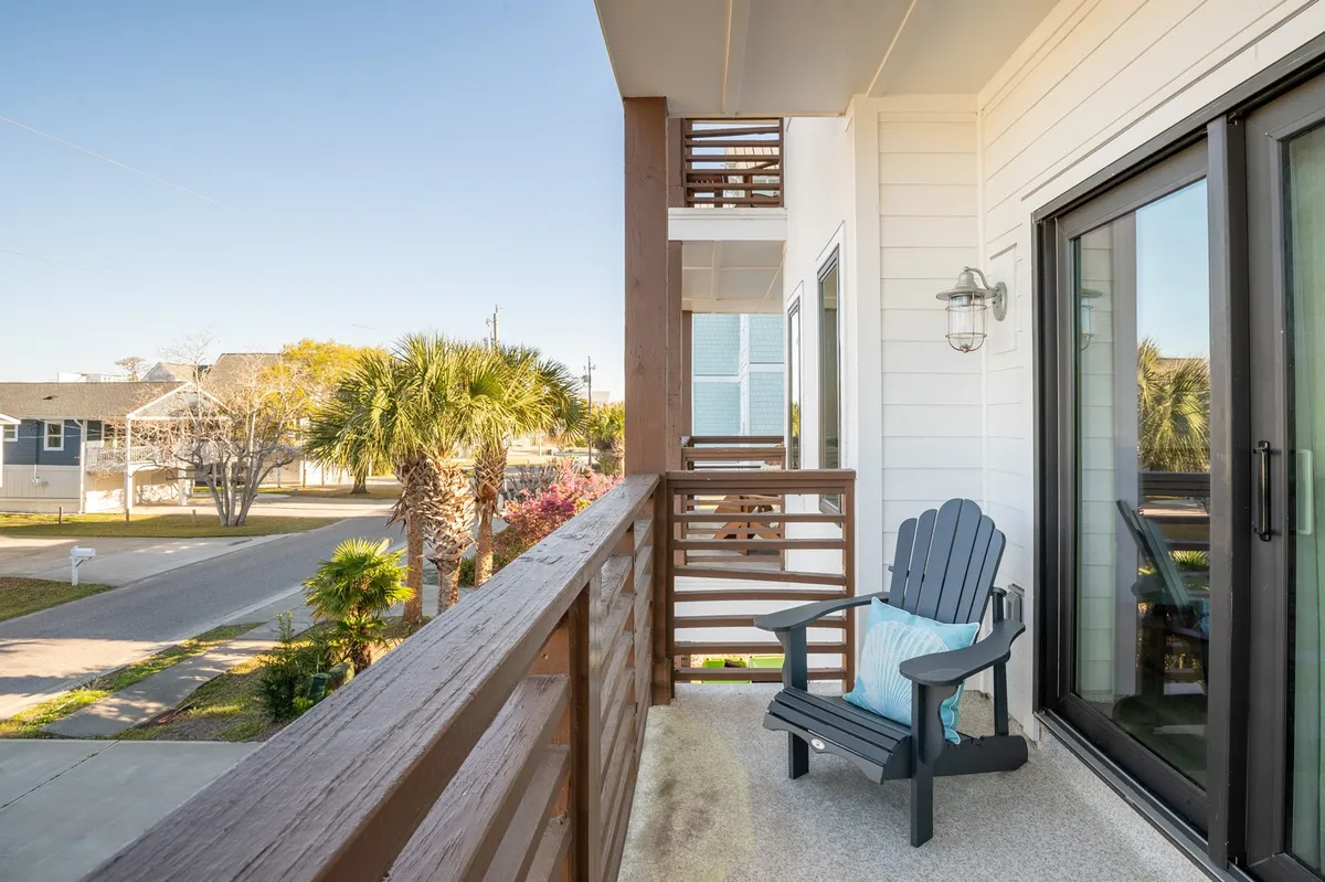 The photo shows an exterior balcony with an Adirondack chair, palm trees, and a sturdy railing. The tranquil setting is perfect for relaxing, enjoying morning coffee, or watching sunsets in the evening. The cozy, private vibe fits both intimate and group moments.