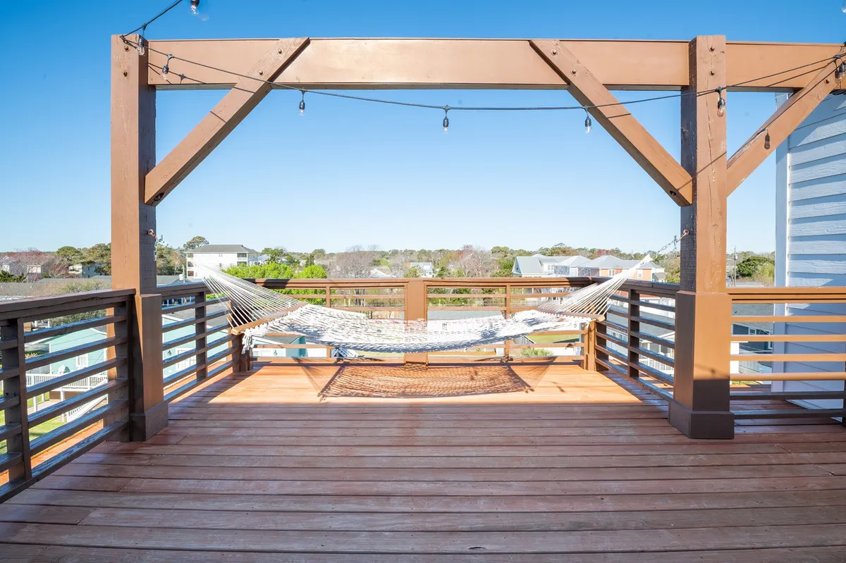 A tranquil exterior scene featuring a hammock set within a wooden structure adorned with string lights. The ambiance is peaceful, ideal for relaxing, reading, or socializing as sunset approaches or under the stars at night.