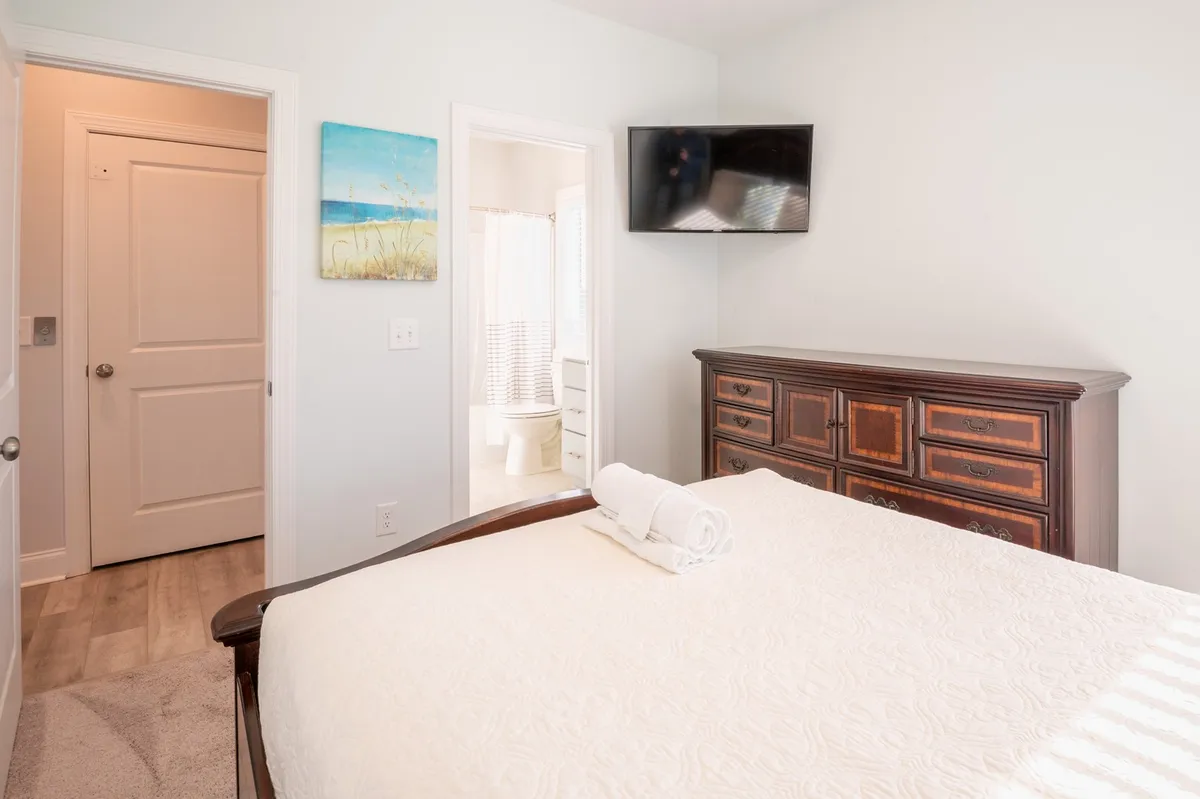 A comfortable bedroom setup with a bed, dresser, TV, and adjoining doorways, bathed in natural light. The room feels spacious yet cozy, ideal for relaxing and enjoying personal time.
