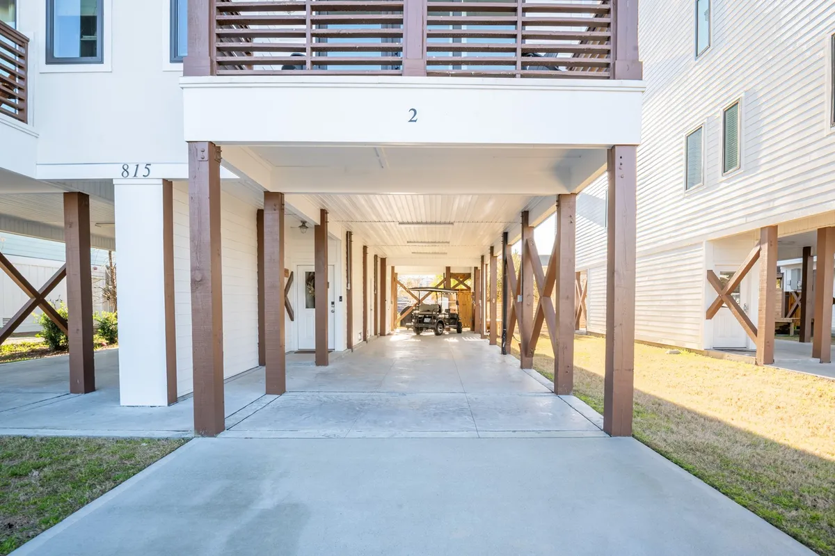 This image shows the ground-level covered parking area beneath the building, supported by sturdy wooden posts. The open space is well-lit and inviting, with ample room for multiple vehicles and easy access to the home. The area conveys a sense of convenience for arrivals and a relaxed vibe for family gatherings or unloading beach gear.