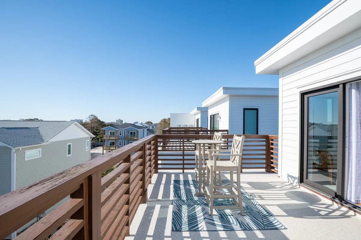 An inviting outdoor seating area with wooden railings, a textured rug, and comfortable chairs, set beneath an open sky. The space is perfect for gathering with friends, relaxing with a drink, or enjoying views of the neighborhood and sunsets.
